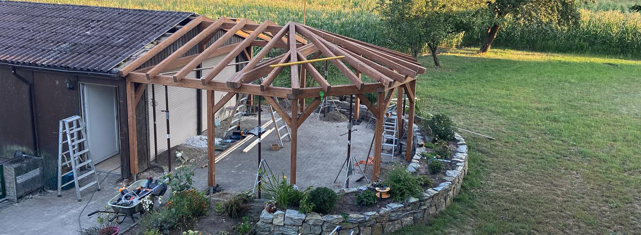 Rohbau einer großen Terrassenüberdachung aus Holz mit Walmdach-Konstruktion – Sparren und Stützpfosten bereits gestellt, Baustelle am Einfamilienhaus – Zimmerei Tragwerk Pietsch aus Steinhagen, Kreis Gütersloh